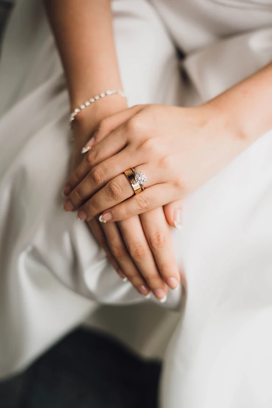A bride's hands with her rings, resting on a white dress