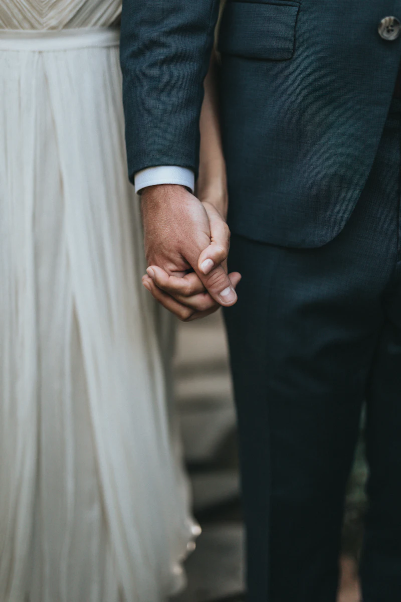 A man in a dark suit holding hands with a woman in a white skirt