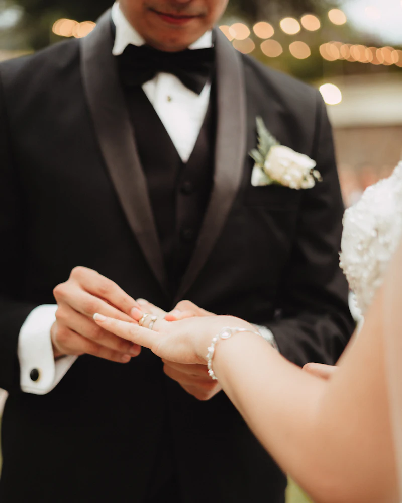 A groom in a tuxedo putting a ring on his bride's finger