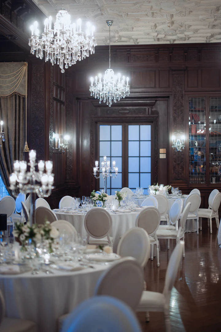 A ballroom with crystal chandeliers and round tables set for dinner