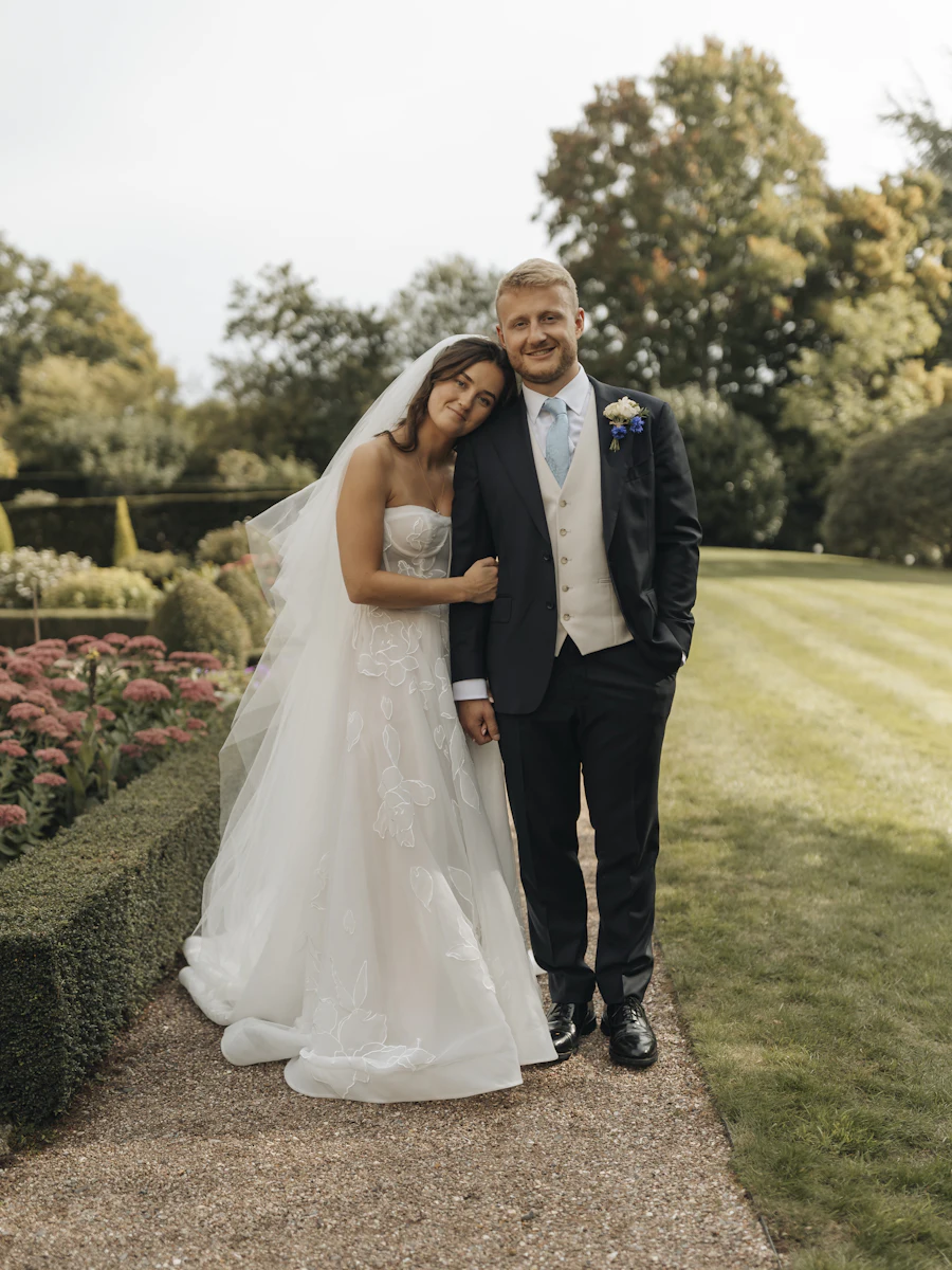 A smiling bride and groom standing together on a garden path