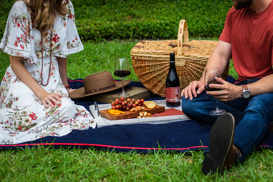 A couple sitting on a picnic blanket in the grass with a basket of food