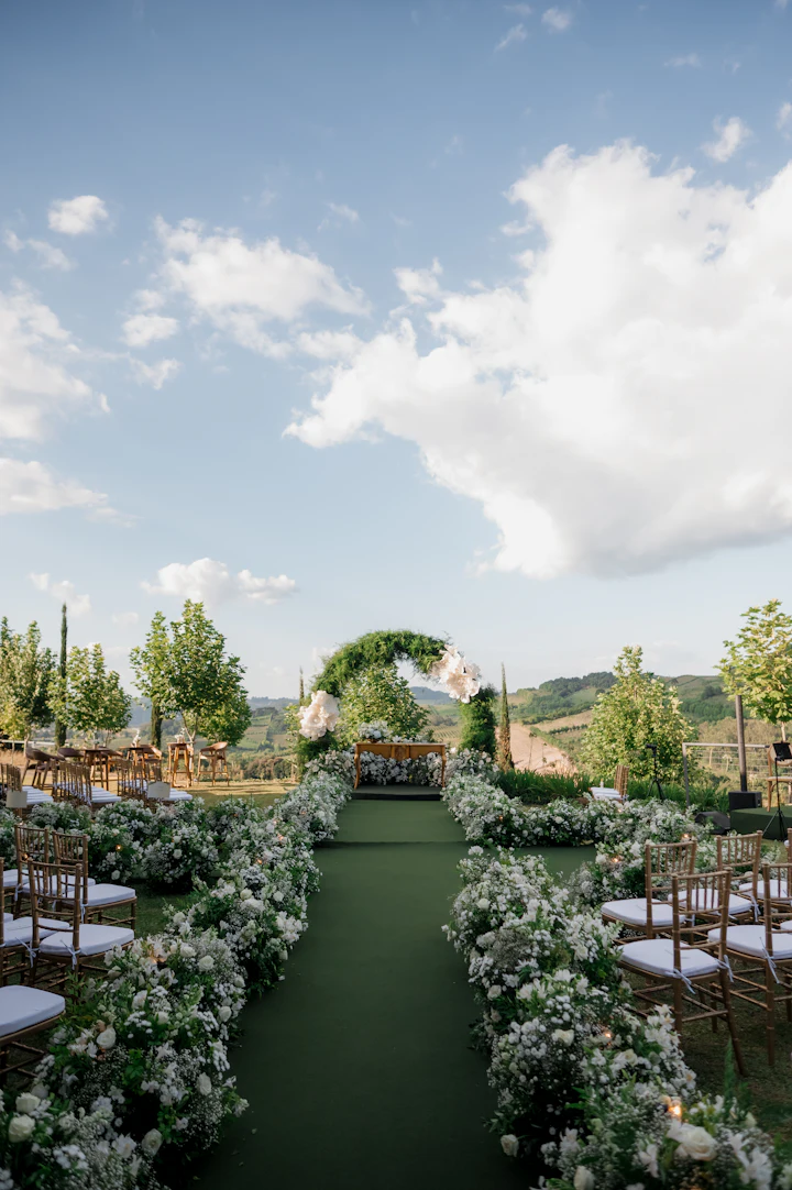 A garden aisle lined with white flowers and wooden chairs under a blue sky