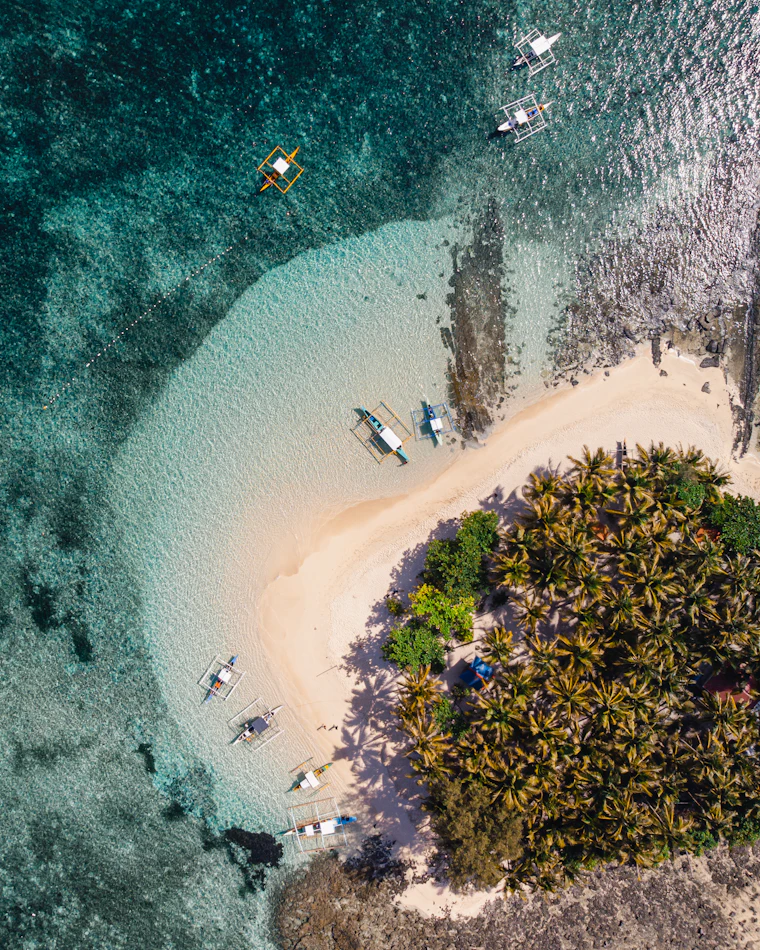 Small boats resting near a white sand beach and green island, seen from above