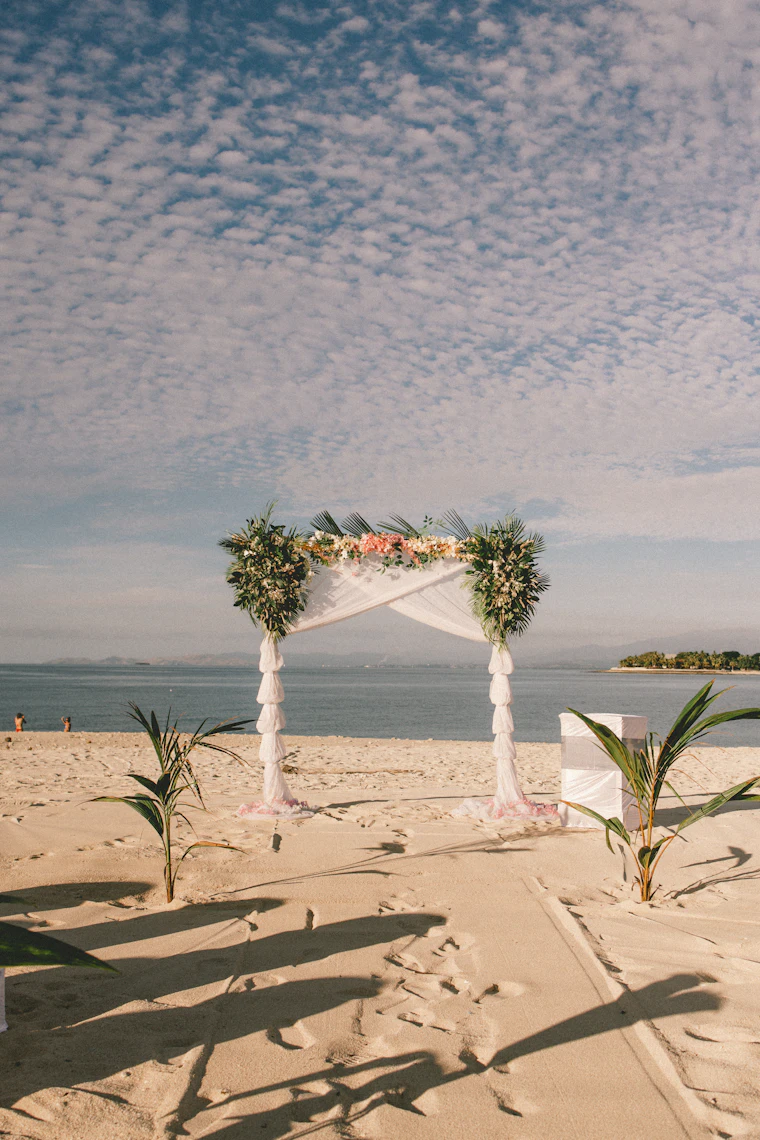 A wedding arch with flowers and greenery on a beach, with an island in the distance