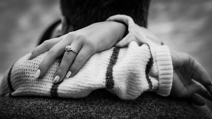 A hand with an engagement ring resting on a sweater, in black and white
