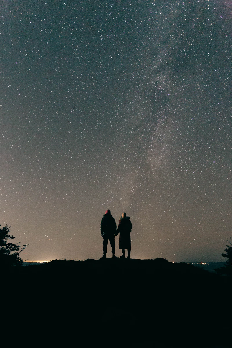 Two people standing on a hilltop under the Milky Way