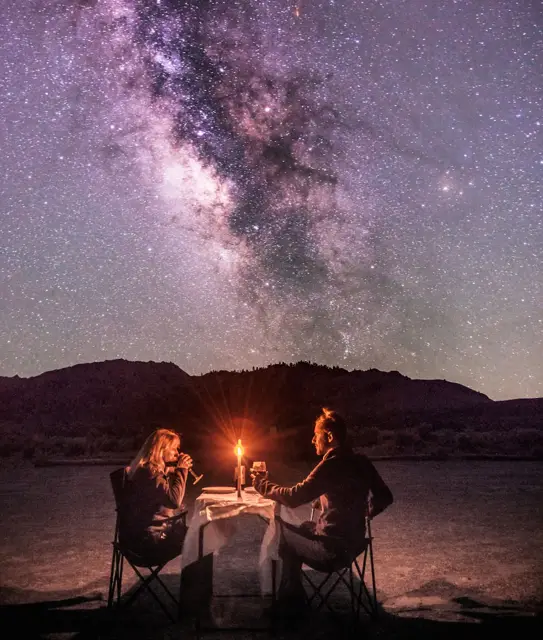 A couple having dinner at a candlelit table under the Milky Way