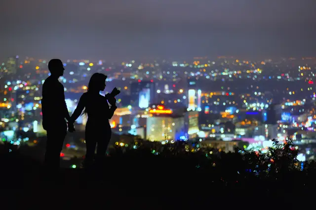 A couple on a hill looking at the city lights at night