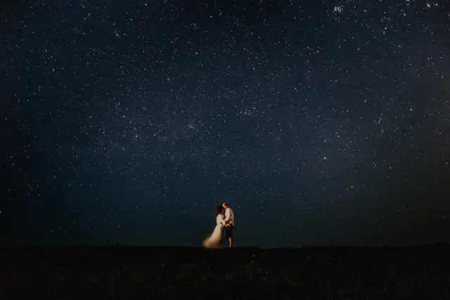 A couple in wedding clothes standing under a sky full of stars