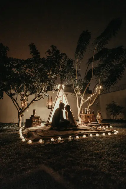 A couple sitting by a small tent lit with string lights at night